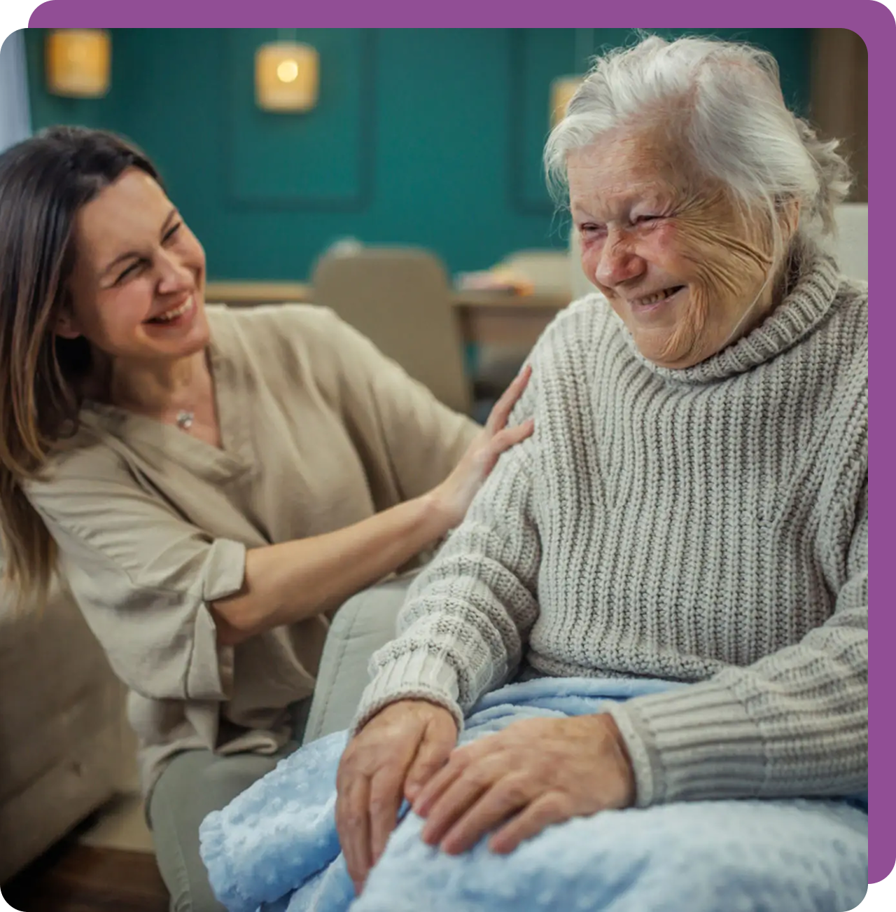 A young woman joyfully interacts with an elderly woman in a cozy setting.