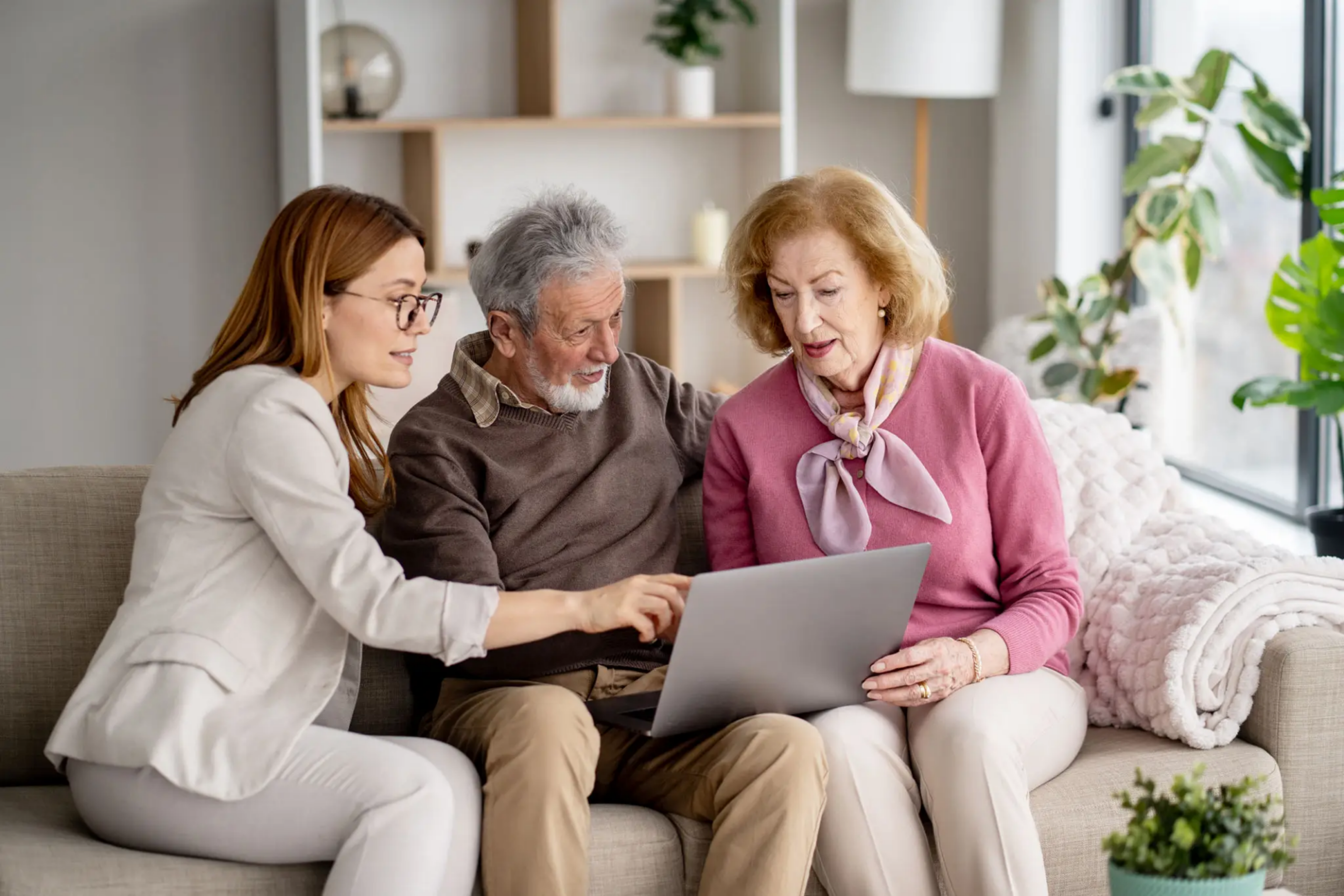 A young woman helps elderly couple with a laptop at home.