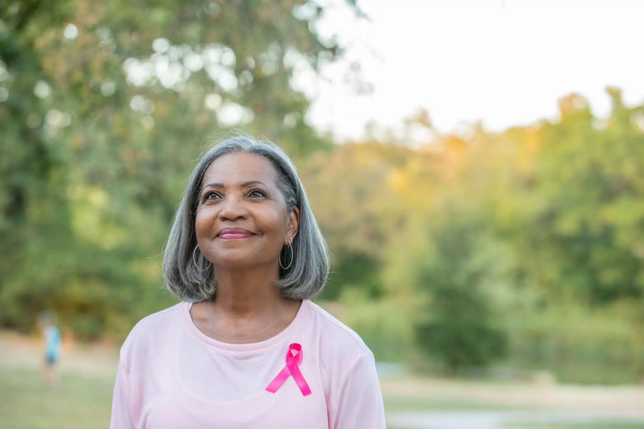 Smiling woman wearing a pink ribbon outdoors.