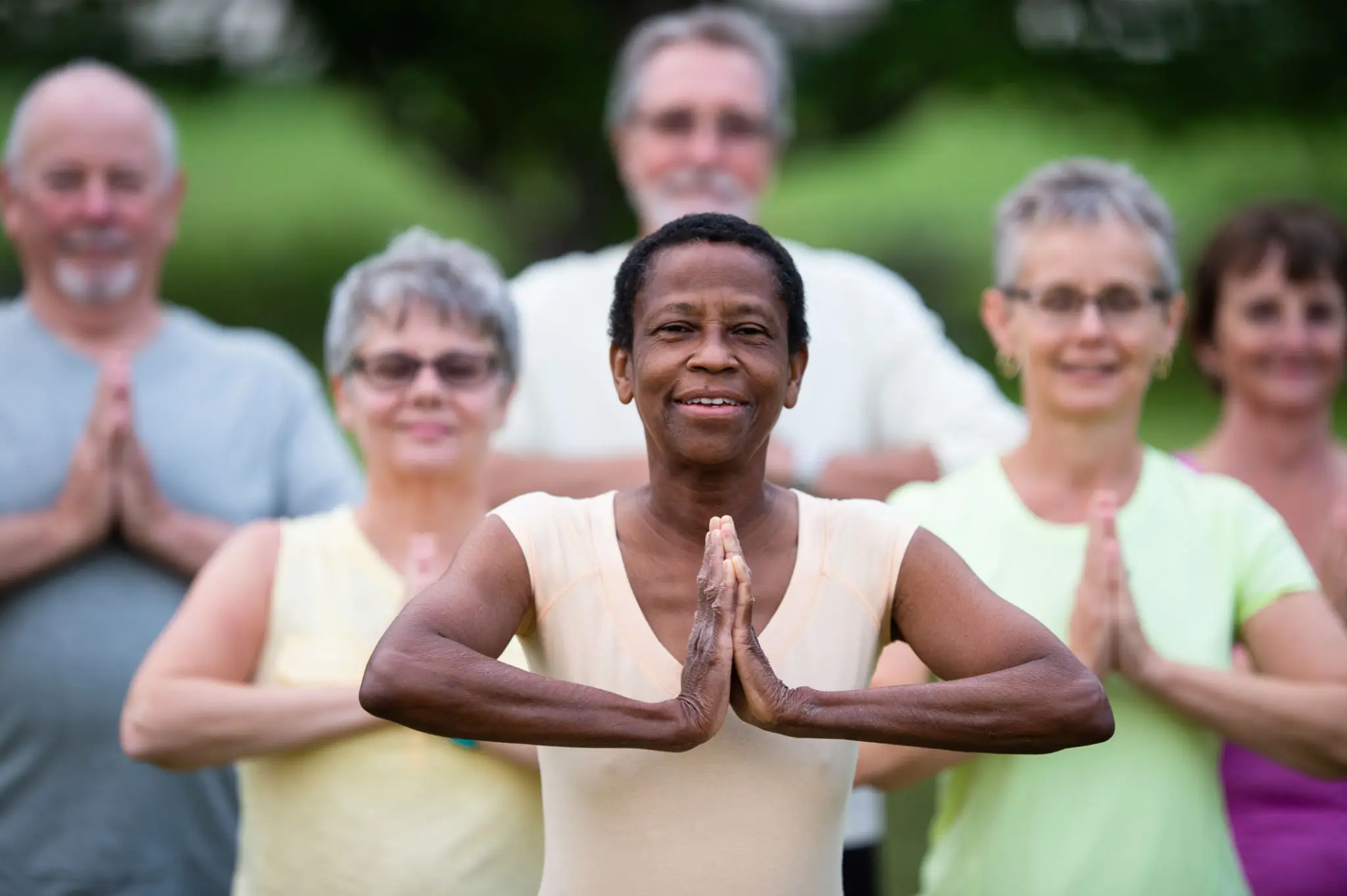 A group practicing yoga outdoors with hands in prayer position.