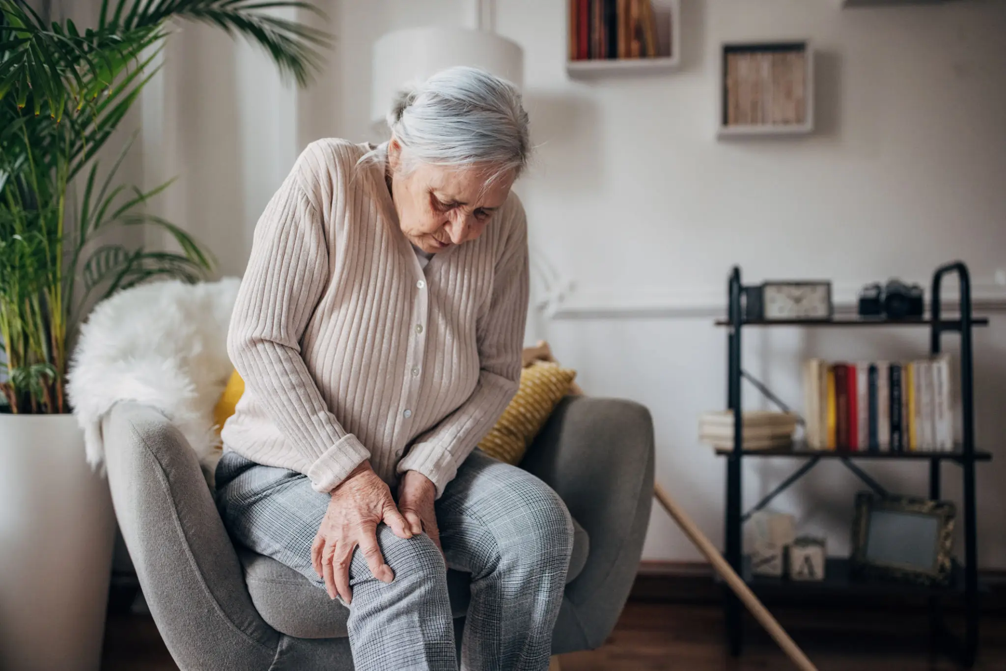 Elderly woman holding her knee in pain while sitting.