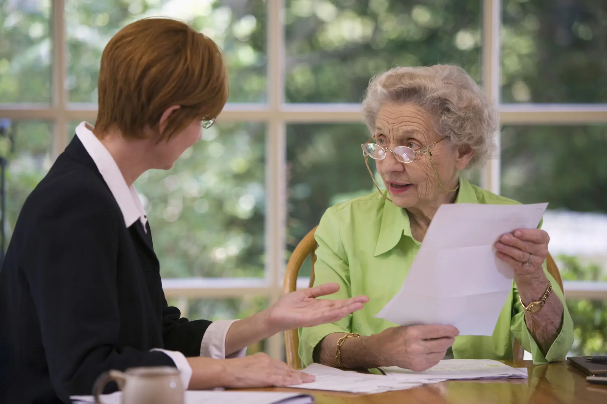 Elderly woman discussing documents with a younger woman indoors.
