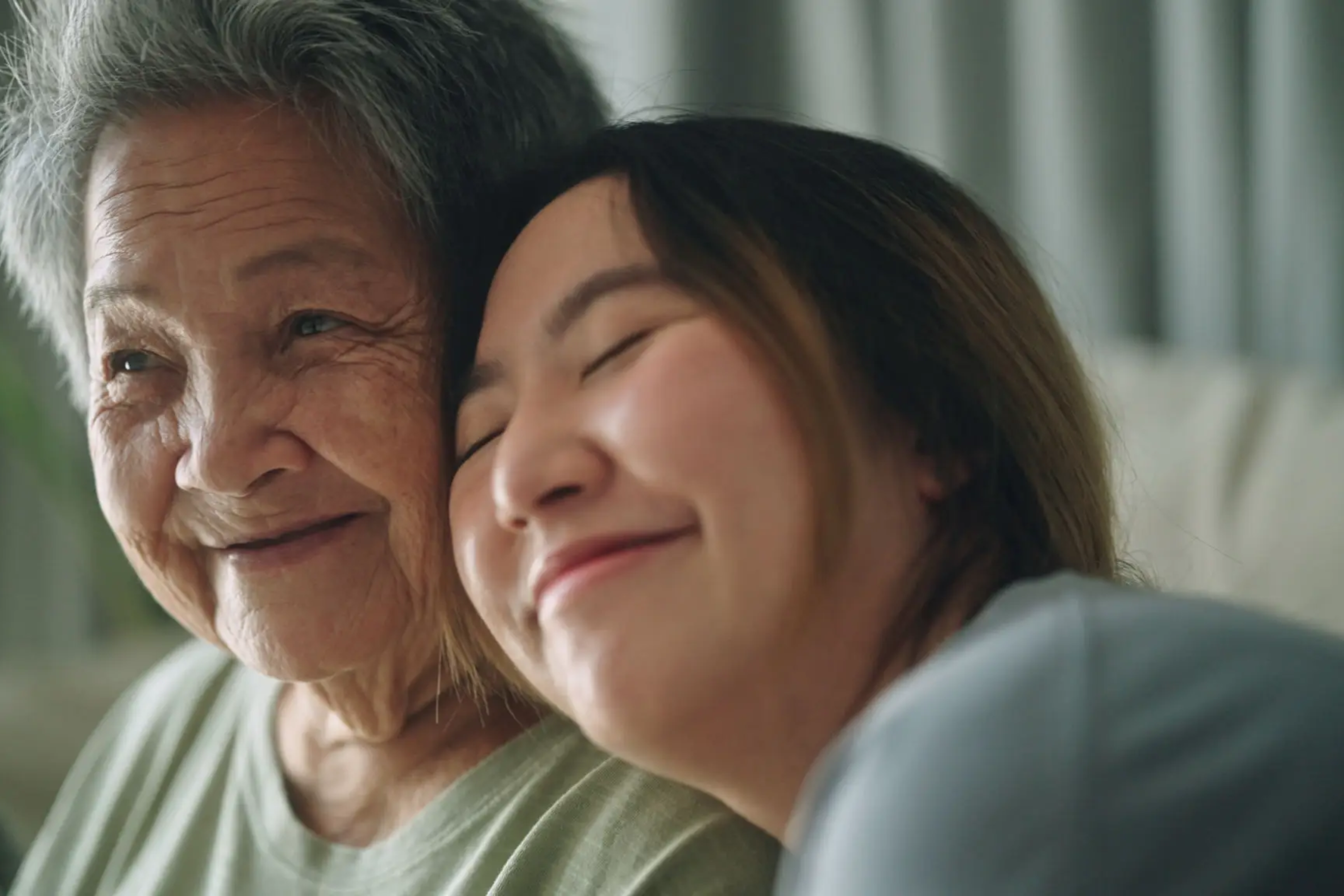 A young woman affectionately leaning on an elderly woman's shoulder.